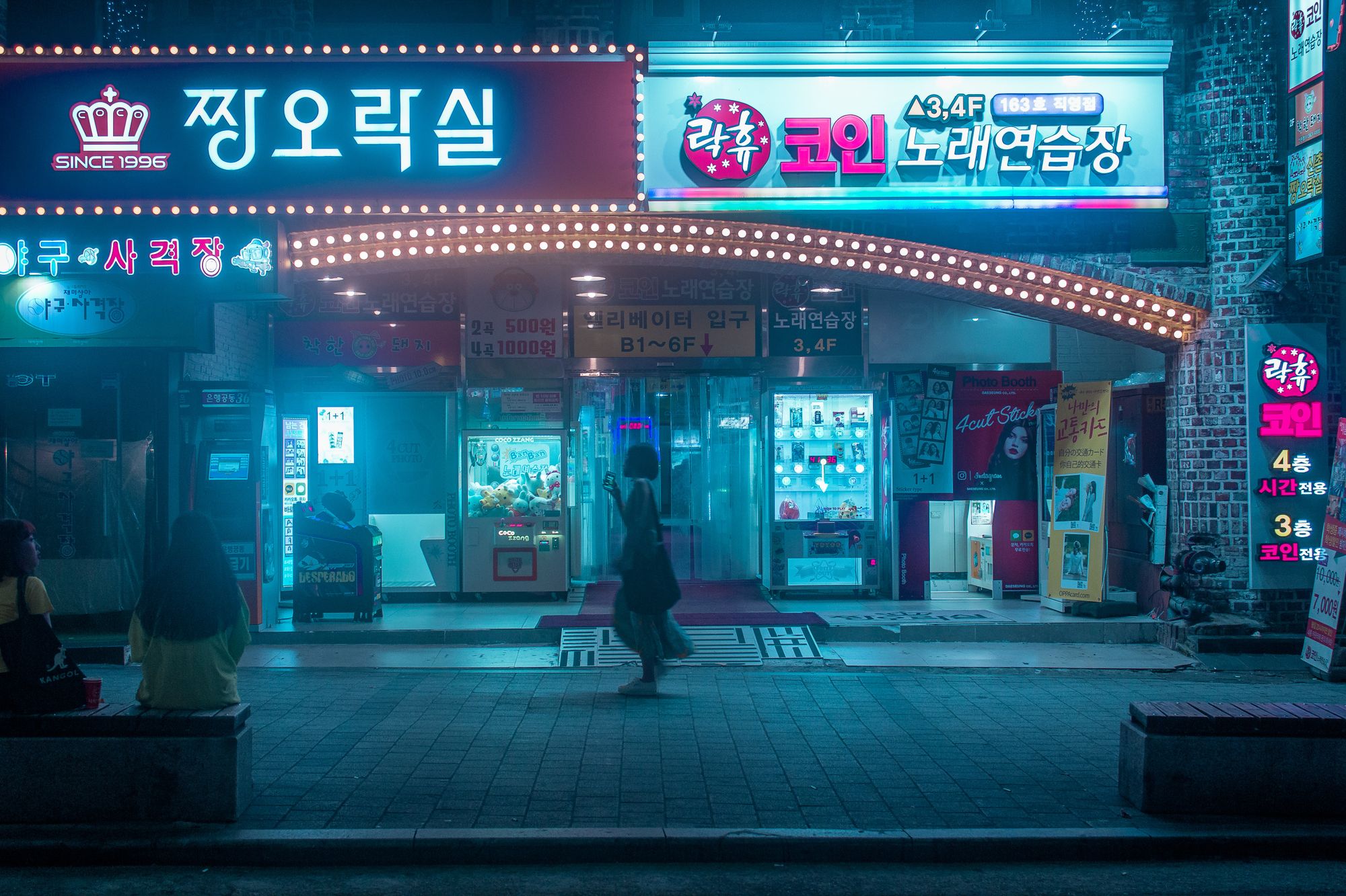 A woman walks through a nighttime urban street in Korea