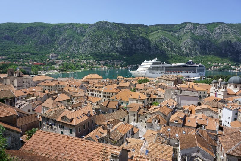 A cruise ship in the Bay of Kotor is foregrounded by houses with orange roofs