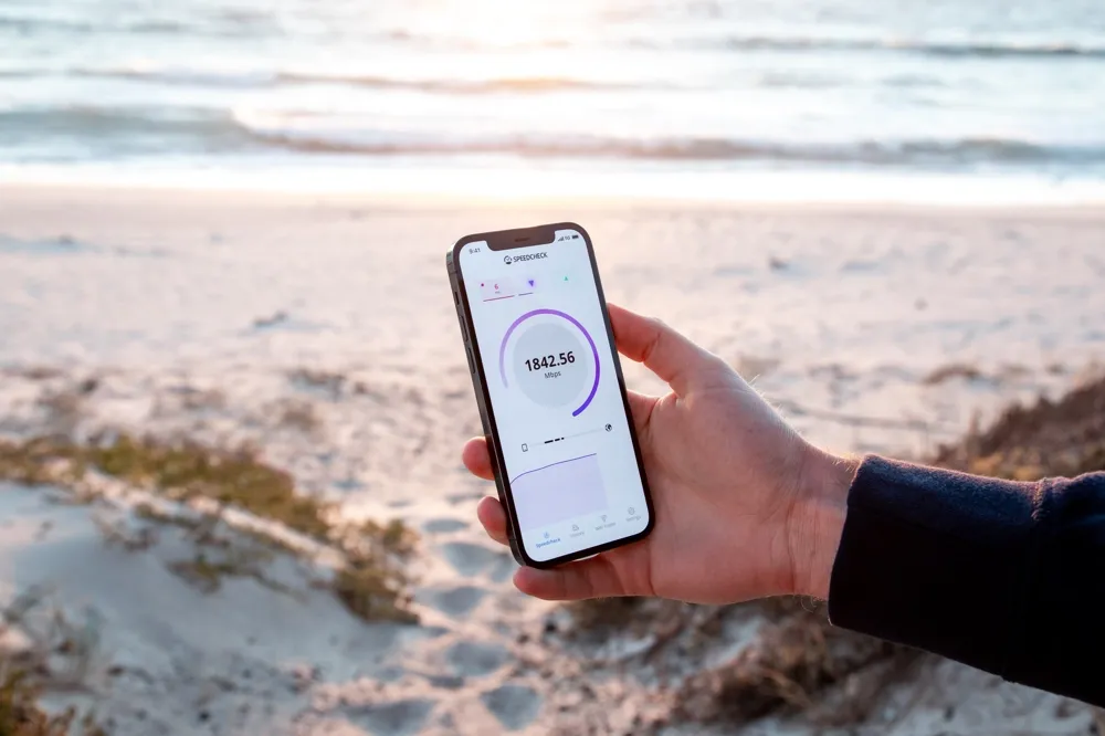 An iPhone with Wi-Fi speed test in someone's hand near a beach