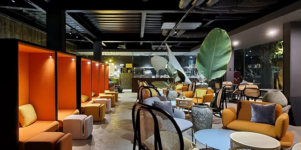 A coworking space with orange booths, tasteful furniture and a large plant and kitchen