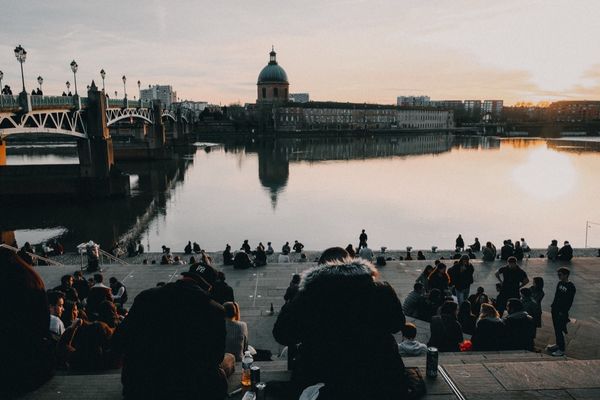 A French riverbank and people on the concrete shore drinking and walking at sunset